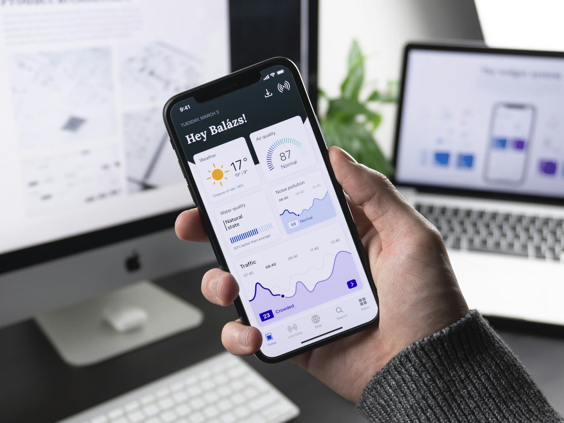Hand holding a phone with a live data app, studio monitors in the background.
