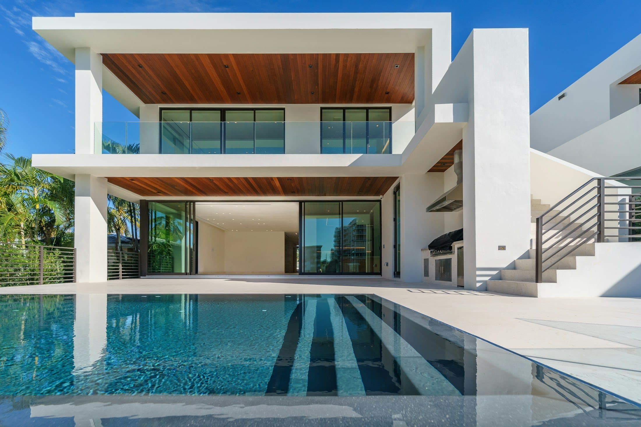White villa with a pool, palms, and an outdoor kitchen under a clear sky.